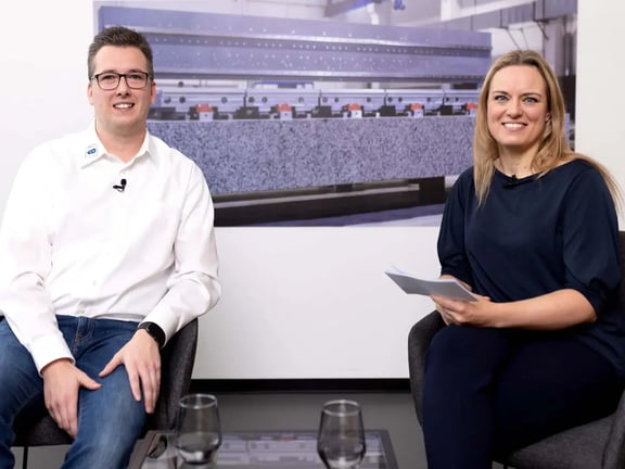 Christopher Reitz von REITZ Natursteintechnik und Moderatorin im Podcast-Studio vor dem Bild eines Granitbauteils; Diskussion über Maschinenbau, Naturstein und hochpräzise Fertigung.