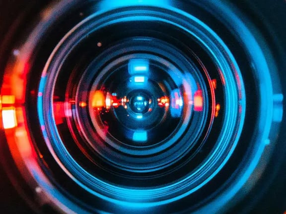 Symbolbild für die optische Industrie: Nahaufnahme einer hochpräzisen Linsen-Optik mit farbigen Lichtreflexionen. Präzision in Messtechnik und Optoelektronik.